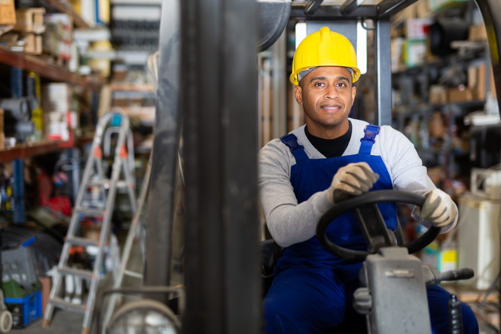 Latin American worker of building materials warehouse working on forklift truck