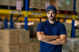 Confident male warehouse worker standing with arms crossed in fa